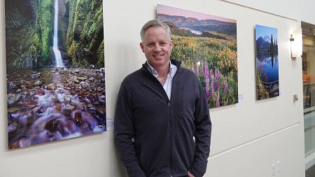 Landscape photographer Mike Putnam stands in front of several of his photographs at the "Flow" event at Oregon Law.