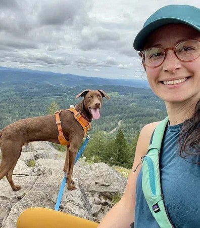 A student hiking in the mountains with a brown dog.