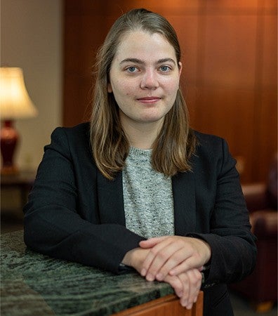 A student with her arm resting on a marble counter wearing a black blazer inside of a conference room.