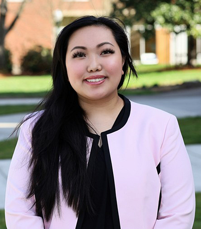 A student wearing a pink cardigan standing outside at the University of Oregon campus.