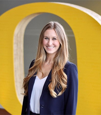 A student standing in front of the yellow "O" logo statue at the University of Oregon.