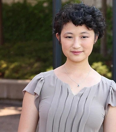 A photo of a student standing outside wearing a gray blouse.