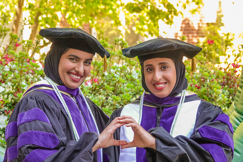 LLM graduates making an O sign with their hands and smiling.