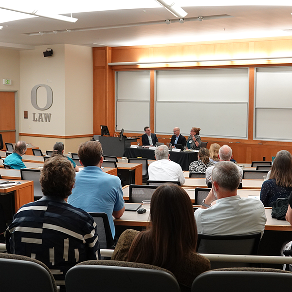 A classroom in the Knight Law Center with three speakers presenting at a desk by the white board and seats with an onlooking audience.