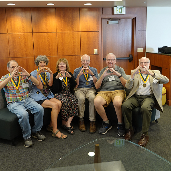 The Class of 1974 reunion sitting down and making an O shape with their hands.