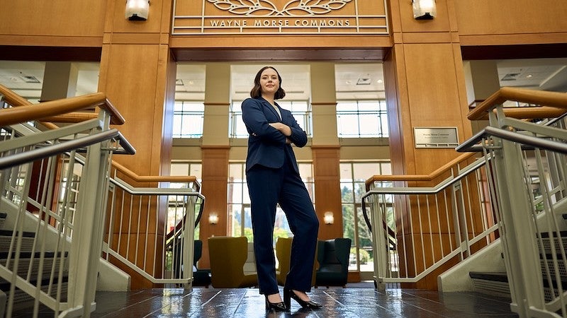 Haley Cook, JD '25, stands at the foot of the stairwell in front of the Wayne Morse Commons sign.