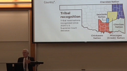 Professor Howard Arnett presents at a podium in front of a PowerPoint slide with a map showing reservation lands of the Seminole Nation, Chickasaw Nation, Choctaw Nation, and Muscogee (Creek) Nation