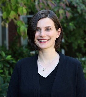 Woman with short brown hair and blue eyes smiling and standing outside the law school