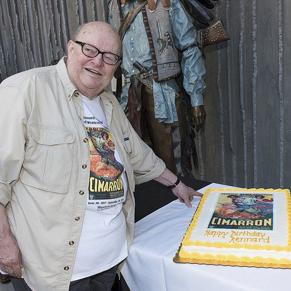 Rennard Strickland standing before a birthday cake featuring his most prized movie poster while wearing a tshirt with the same movie poster printed on the front
