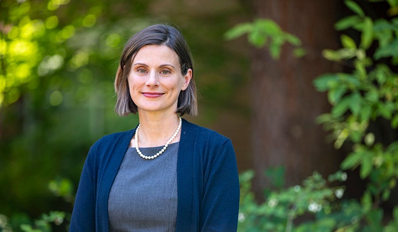 Professor Jen Reynolds smiling at the camera with redwood and green foliage in background
