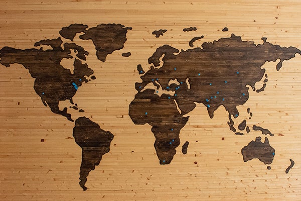 world map burned onto a wooden board with blue marker pins 