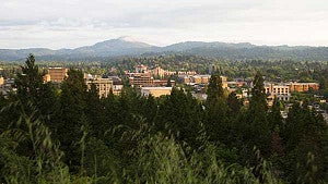Skyline of Eugene with trees in the foreground and hills in the background