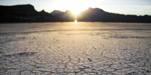 out-of-focus sunrise behind shady ridge with cracked desert soil coming into focus at bottom