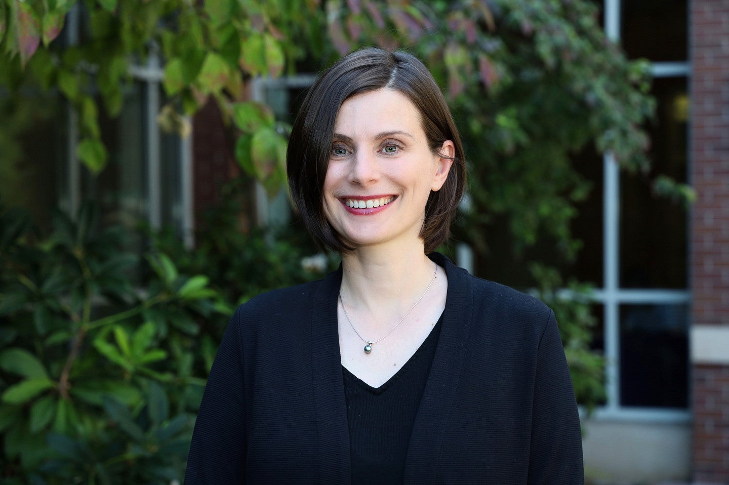 Woman with short brown hair and blue eyes smiling and standing outside the law school