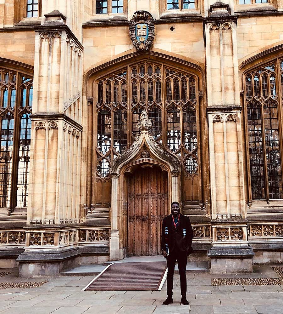 Akinbosade Adedayo standing in front of an exterior door outside the Divinity School at Oxford University