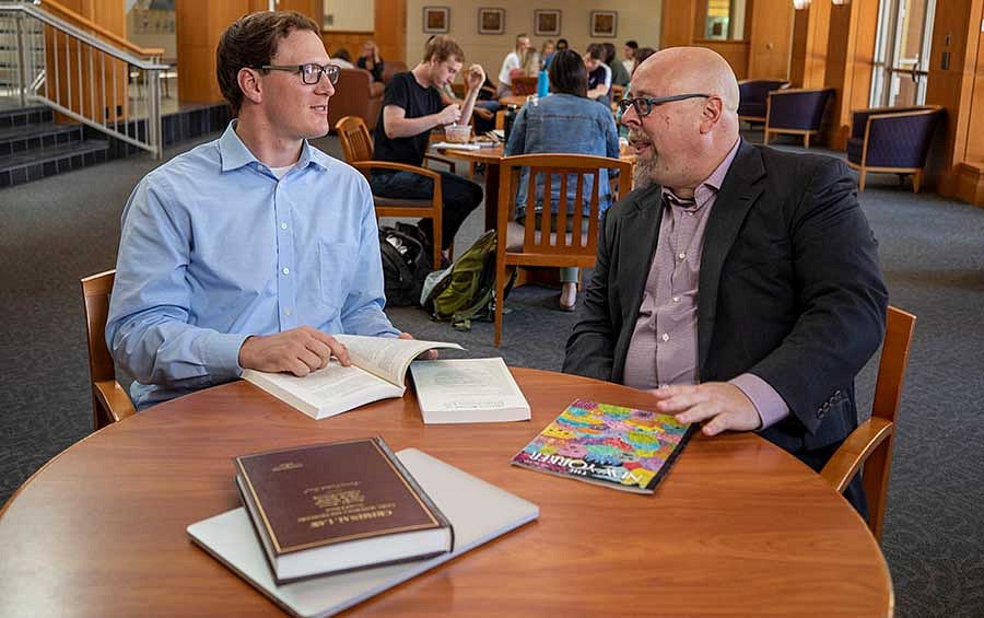 A student and professor having a discussion at a table in the Knight Law Center