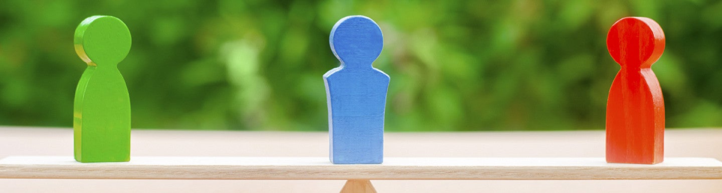three wooden figures on a seesaw, one red and one green on opposing sides and one blue, in the middle balancing.