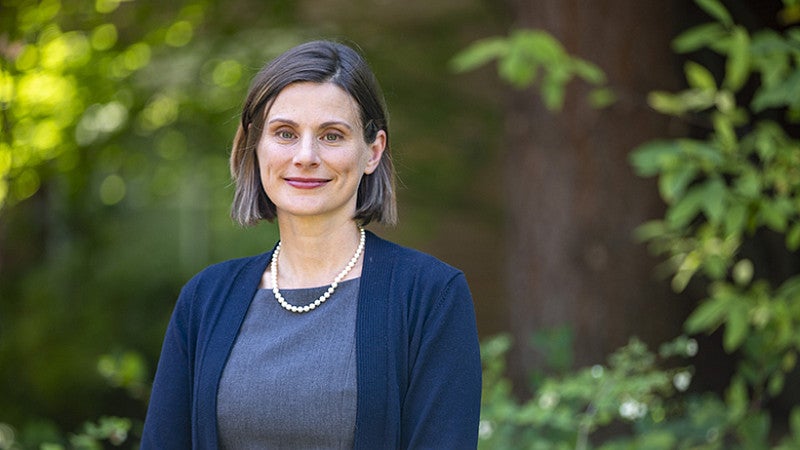 Professor Jen Reynolds smiling at the camera with redwood and green foliage in background