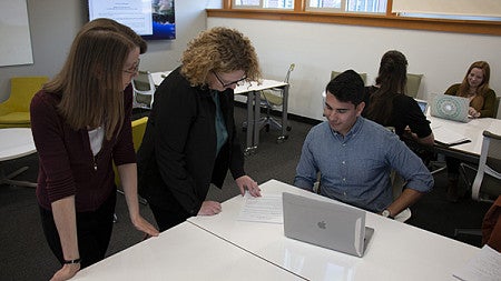 two professors leaning over to help a student during a clinic