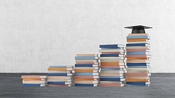 increasing levels of book towers with a graduation cap on the tallest one.